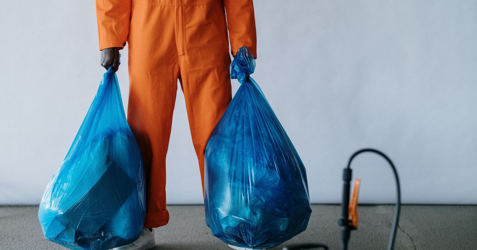 Sanitation worker in orange overalls holding blue trash bags indoors for waste management.